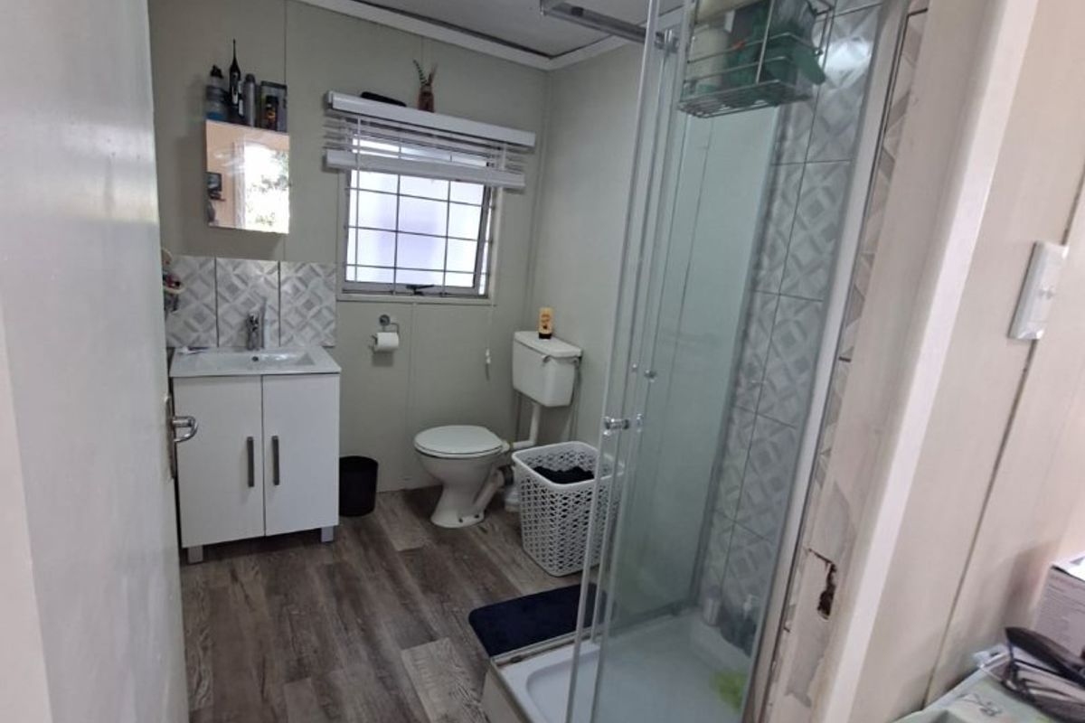 A functional bathroom featuring a glass shower enclosure, vanity cabinet with basin, toilet, and wood-look laminate flooring.