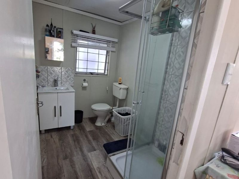 A functional bathroom featuring a glass shower enclosure, vanity cabinet with basin, toilet, and wood-look laminate flooring.