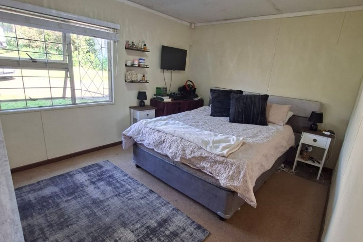 A bedroom featuring carpet flooring, ceiling tiles, and a window with security bars, offering a functional space in need of cosmetic updates.