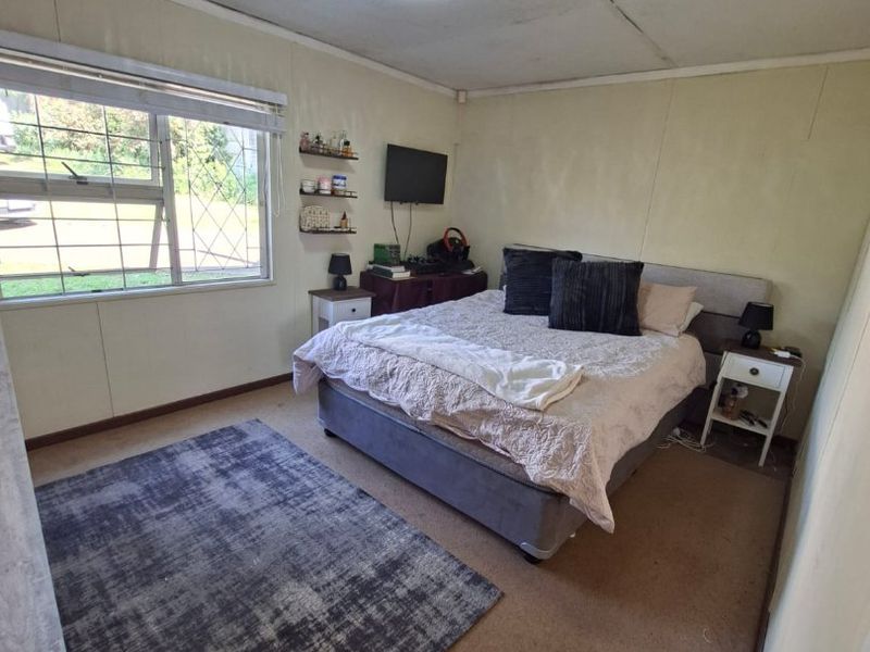 A bedroom featuring carpet flooring, ceiling tiles, and a window with security bars, offering a functional space in need of cosmetic updates.