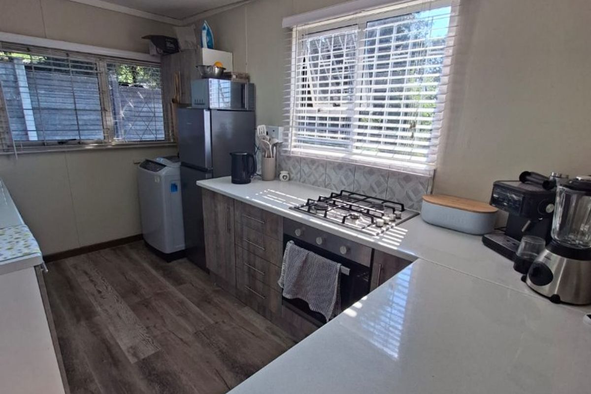 A functional kitchen featuring wood-look cabinetry, a gas hob, built-in oven, tiled backsplash, and laminate flooring with ample natural light from dual windows.