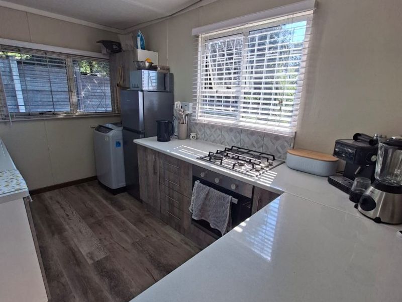 A functional kitchen featuring wood-look cabinetry, a gas hob, built-in oven, tiled backsplash, and laminate flooring with ample natural light from dual windows.