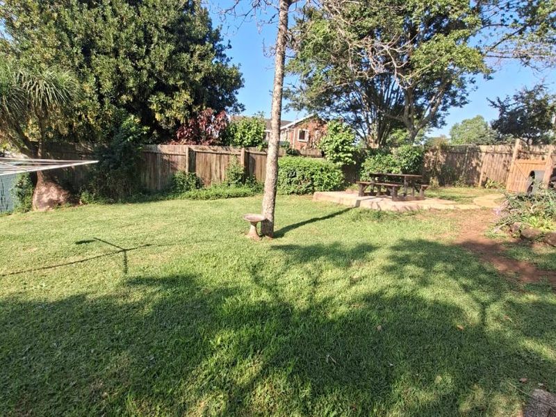 A private backyard featuring a well-maintained lawn, mature trees, and perimeter wooden fencing, providing a peaceful outdoor space.