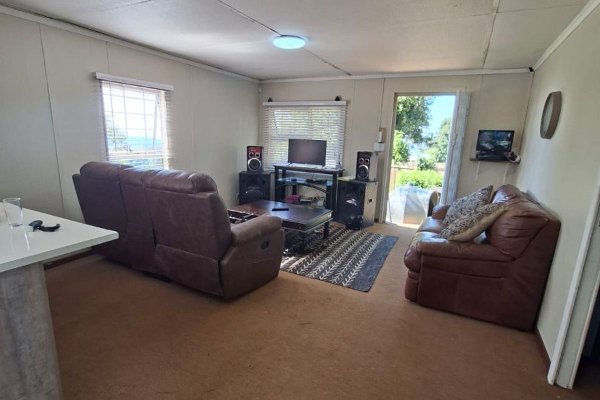A living room area featuring carpet flooring, ceiling tiles, and direct access to an outdoor space through a glass door.