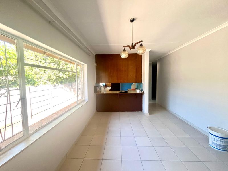 An open-plan living and kitchen area featuring tiled flooring, a breakfast bar, and built-in cabinetry, offering a blank canvas for renovation.