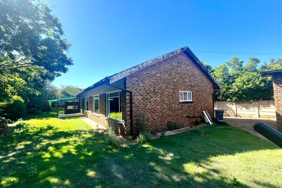 Rear view of a face brick house featuring metal window frames with security bars, set on a large plot with a lawn and boundary wall.