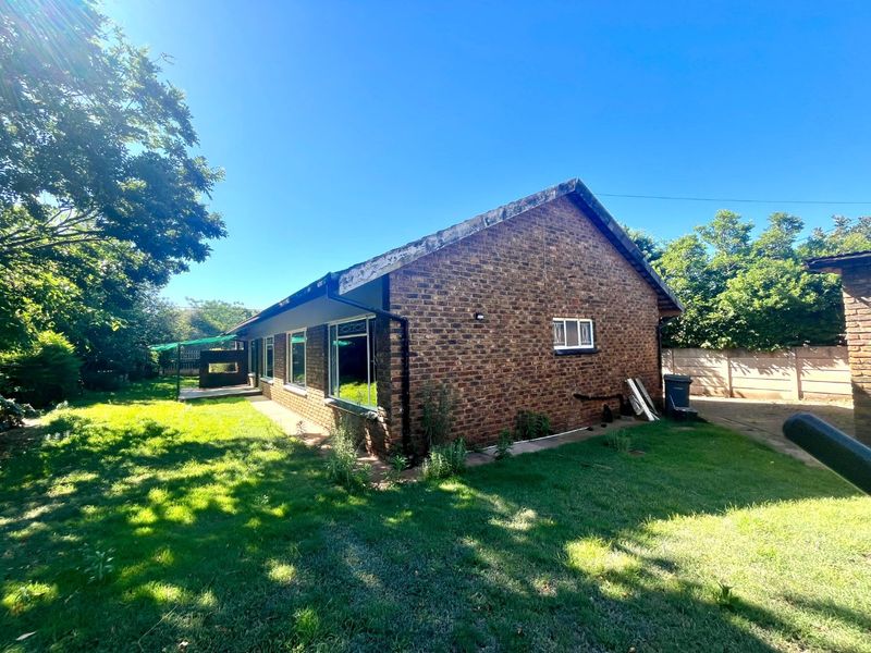 Rear view of a face brick house featuring metal window frames with security bars, set on a large plot with a lawn and boundary wall.