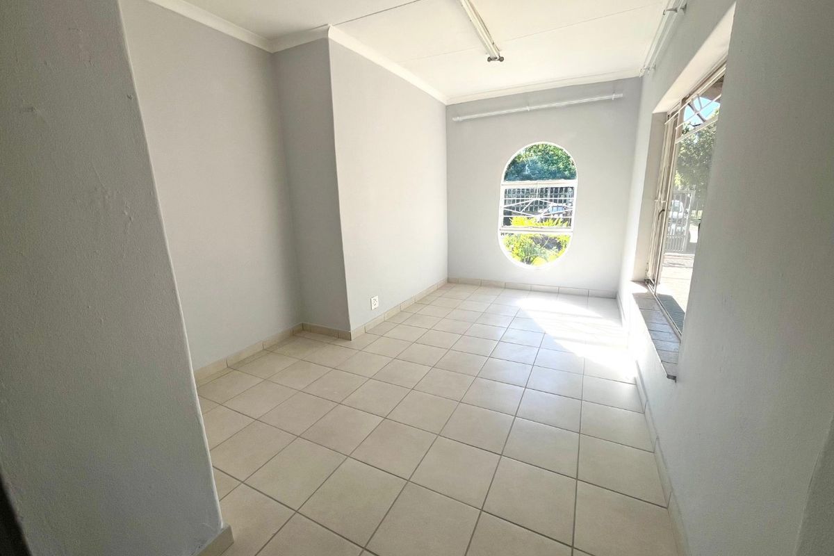 A bright, empty bedroom featuring neutral tiled flooring, a unique arched window, and large sliding windows that provide ample natural light.