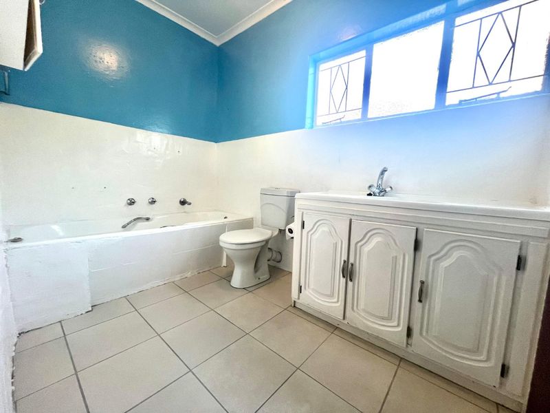 A functional bathroom featuring a built-in bathtub, toilet, and vanity cabinet with basin, finished with tiled flooring and natural light from a window.