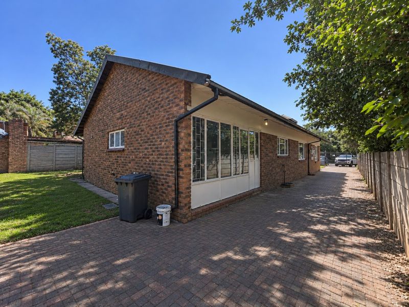 A side view of a face brick house featuring a paved driveway, metal window frames, and a surrounding precast concrete boundary wall.