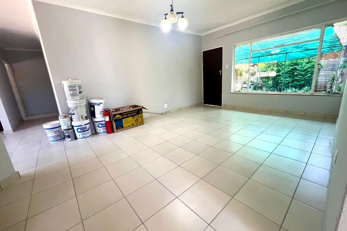 A bright, empty living room featuring neutral tiled flooring, a large window, and a central ceiling light fixture.