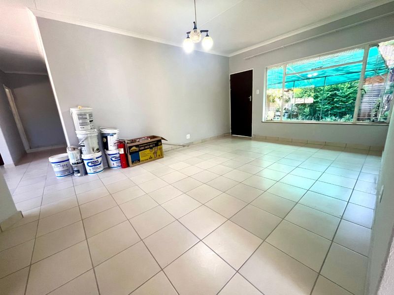 A bright, empty living room featuring neutral tiled flooring, a large window, and a central ceiling light fixture.