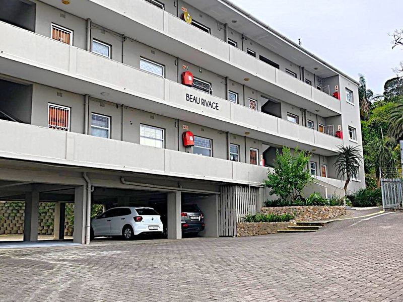 Exterior view of the Beau Rivage apartment complex featuring a paved driveway, covered parking area, and multi-level balconies.