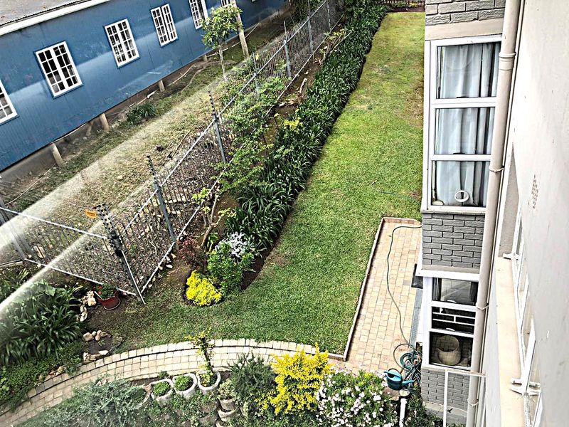 An elevated view of the rear garden featuring a well-maintained lawn, paved pathway, and secure perimeter fencing.