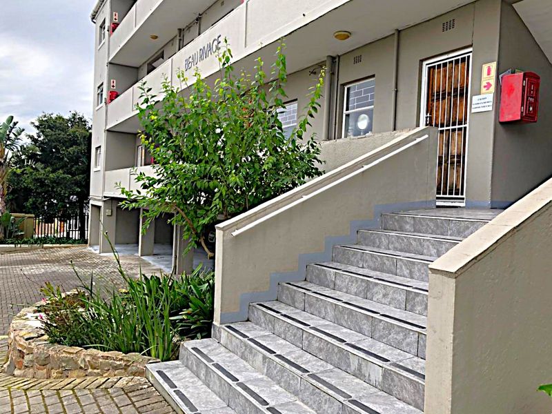 Exterior view of the apartment building entrance featuring a tiled staircase, security gate, and paved driveway area.