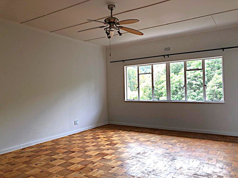 Spacious bedroom featuring original parquet flooring, a ceiling fan, and large windows providing natural light and garden views.