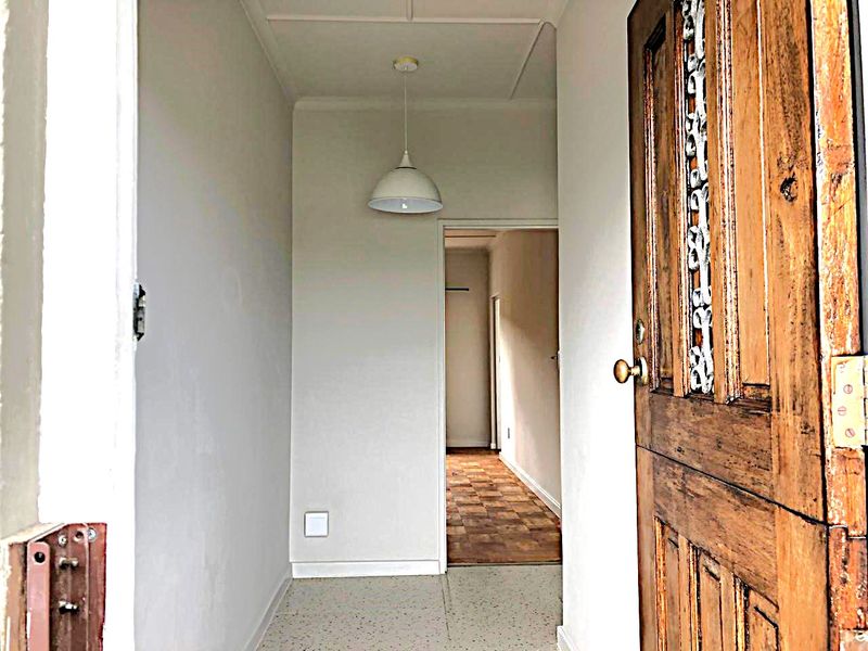 Entrance hallway featuring a classic timber door, terrazzo flooring, and a pendant light fixture, leading into a secondary space with parquet flooring.