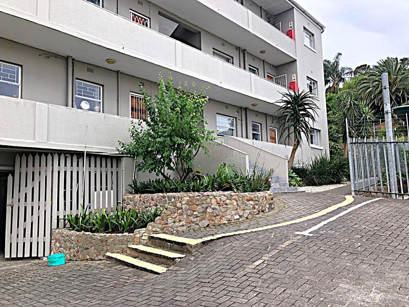 Exterior view of an apartment building featuring a paved driveway, stone retaining wall, and multi-level balconies with security features.