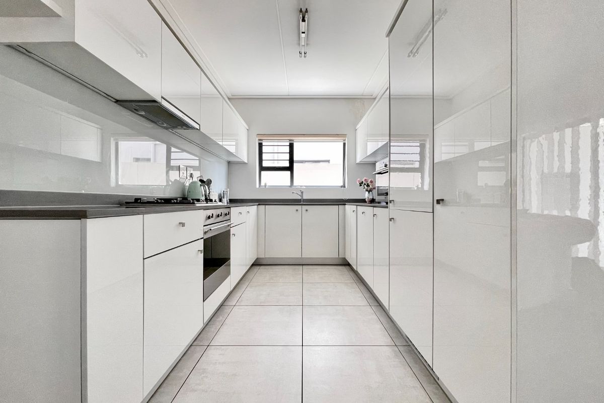 Modern galley-style kitchen featuring high-gloss white cabinetry, stone countertops, integrated oven, gas hob, and tiled flooring with a functional layout.