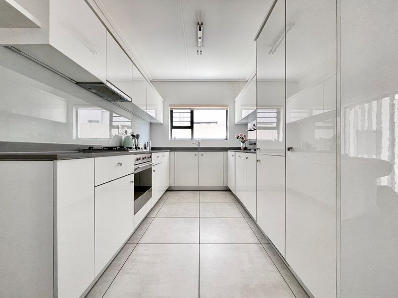 Modern galley-style kitchen featuring high-gloss white cabinetry, stone countertops, integrated oven, gas hob, and tiled flooring with a functional layout.
