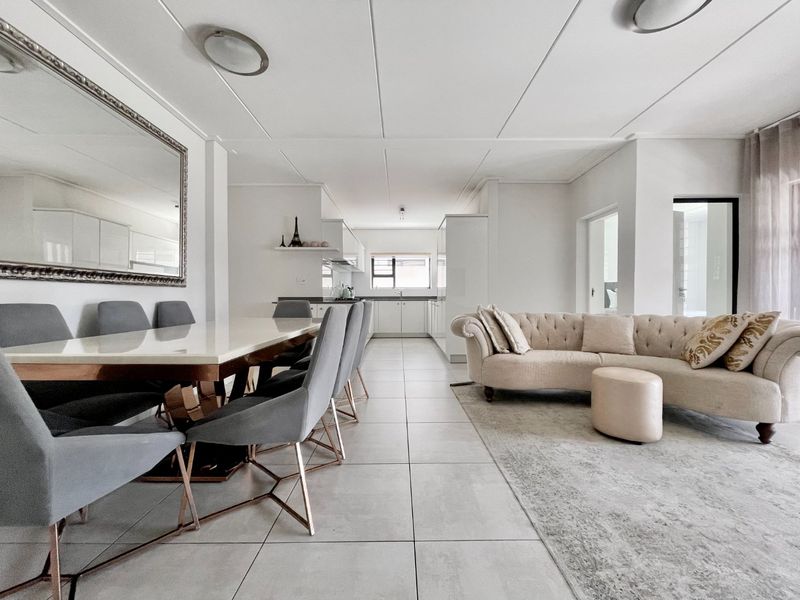 A spacious open-plan living and dining area featuring modern tiled flooring, neutral finishes, and a seamless transition into a functional kitchen space.