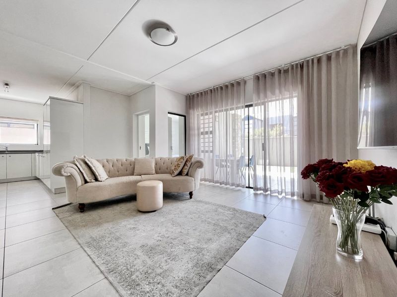 Bright open-plan living area featuring neutral tiled flooring and large sliding glass doors that provide seamless access to the outdoor patio space.