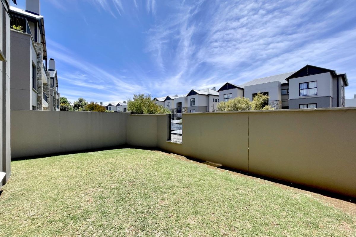 A private rear garden area featuring a well-maintained lawn enclosed by a solid boundary wall within a modern apartment complex.