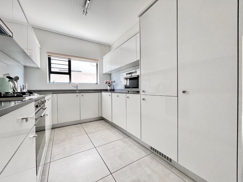 Modern kitchen featuring high-gloss white cabinetry, integrated appliances including an oven and microwave, gas hob, and neutral tiled flooring.