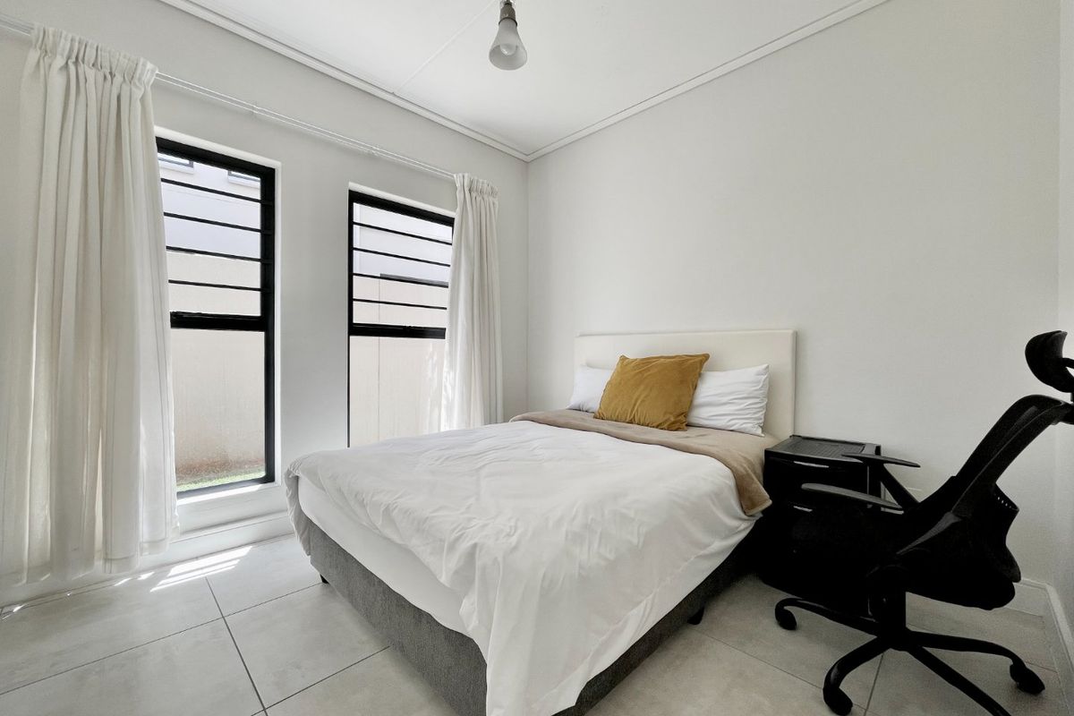 A bright bedroom featuring neutral tiled flooring, clean white walls, and dual windows with black frames, providing ample natural light.