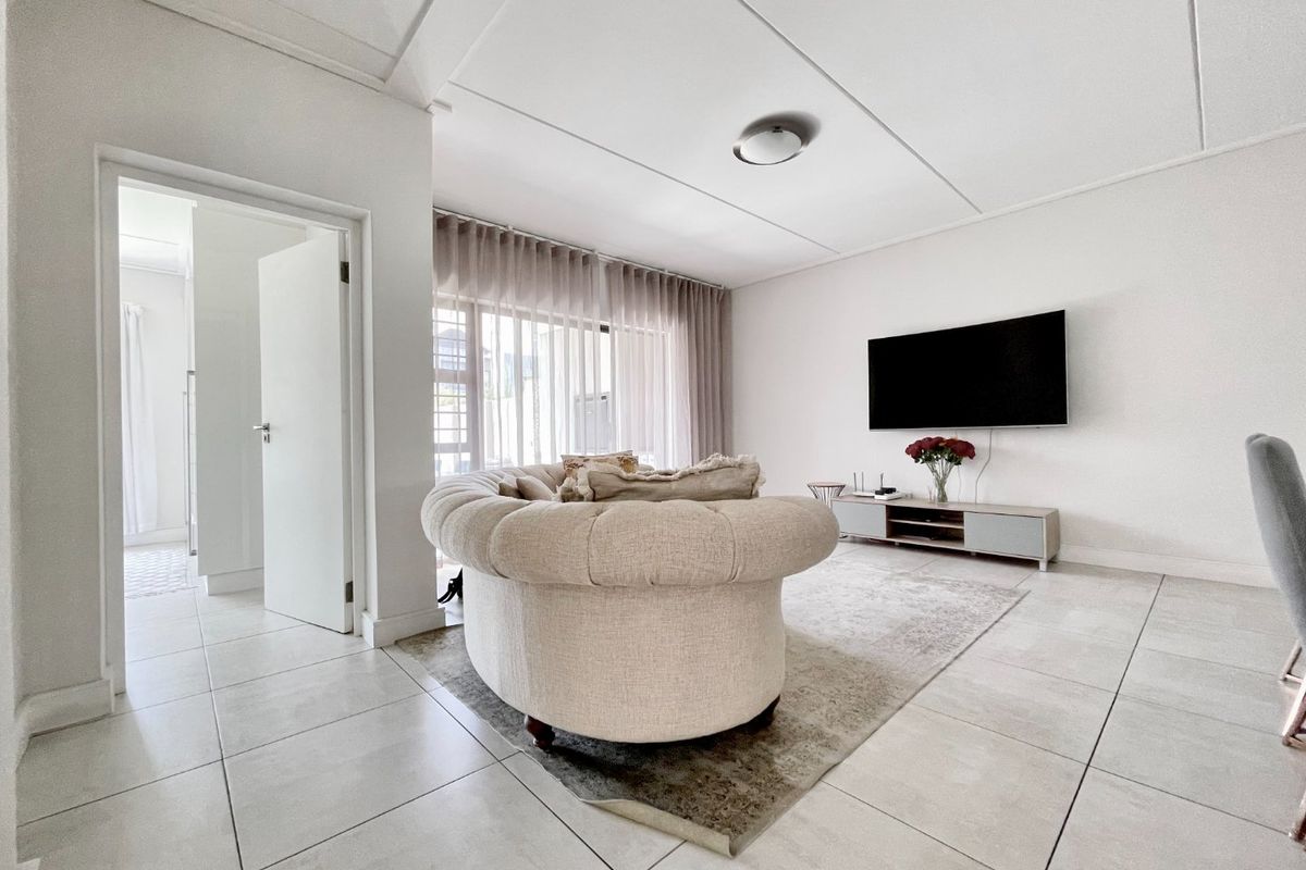 A bright and modern living room featuring large format floor tiles, neutral walls, and a clean, minimalist aesthetic with direct access to an adjacent room.