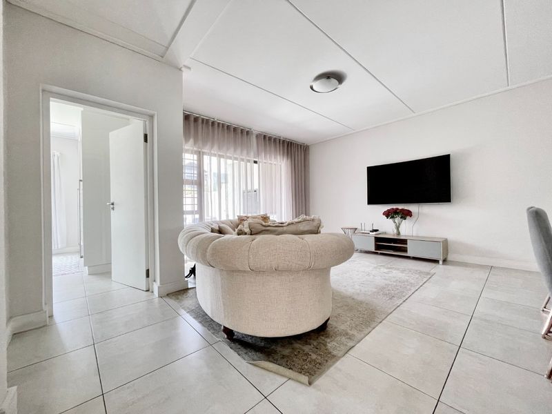 A bright and modern living room featuring large format floor tiles, neutral walls, and a clean, minimalist aesthetic with direct access to an adjacent room.