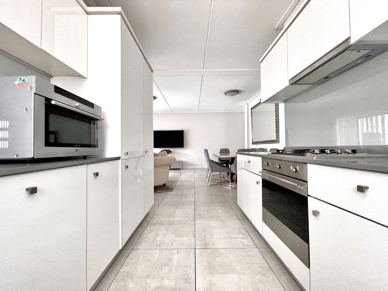 Modern open-plan kitchen featuring sleek white cabinetry, integrated appliances, and tiled flooring, flowing seamlessly into the adjacent living and dining area.
