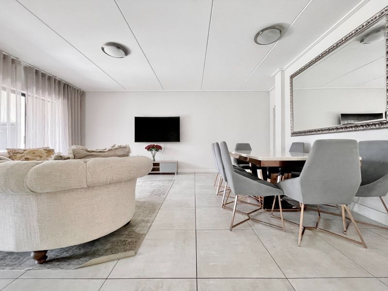 Spacious open-plan living and dining area featuring neutral tiled flooring, modern recessed ceiling lighting, and a large decorative wall mirror.