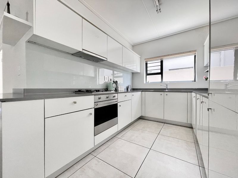 Modern kitchen featuring white high-gloss cabinetry, grey countertops, integrated oven and hob, and large format floor tiles.