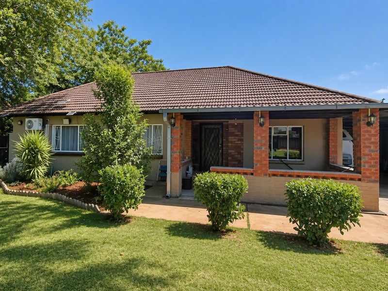Front view of a single-story brick house featuring a covered patio, tiled roof, and established garden.