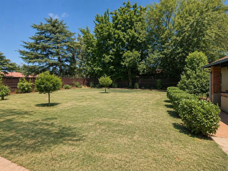 A well-maintained, spacious backyard featuring a large lawn, established trees, and perimeter fencing, providing a private outdoor area.