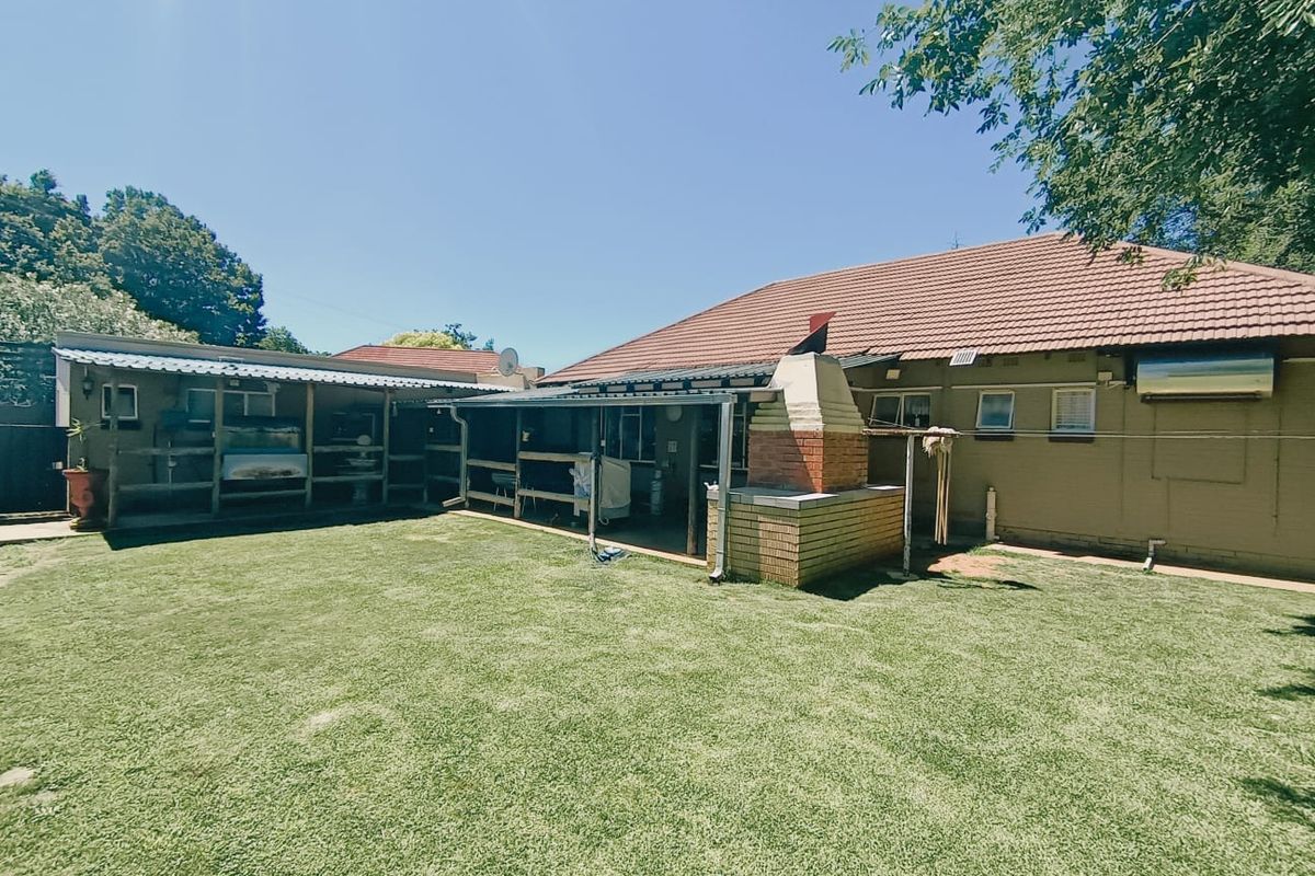 Rear view of the property featuring a spacious lawn, a covered patio area, and a built-in brick braai facility.
