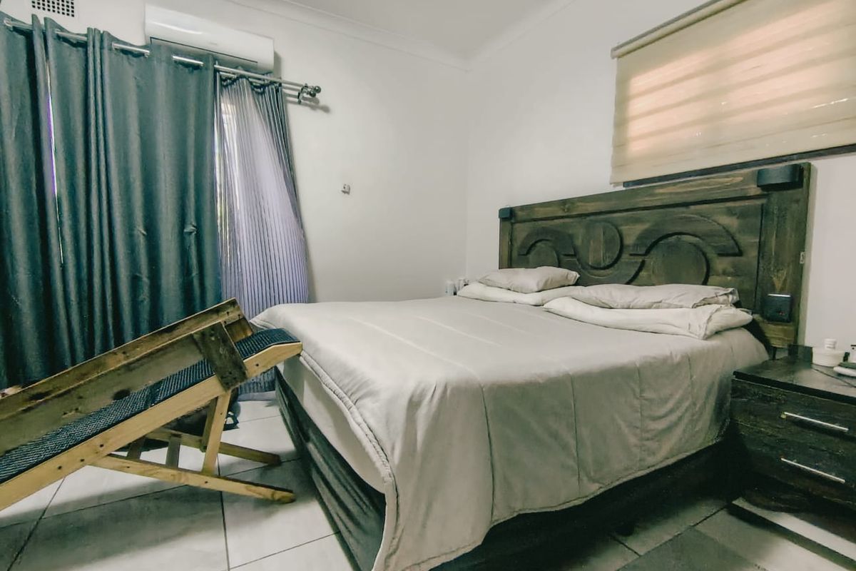 A functional bedroom featuring tiled flooring, an installed air conditioning unit, and window treatments including roller blinds and curtain rails.