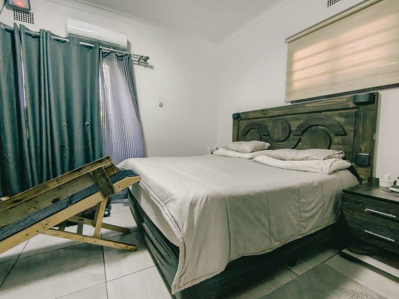 A functional bedroom featuring tiled flooring, an installed air conditioning unit, and window treatments including roller blinds and curtain rails.