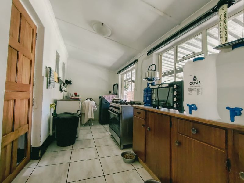 A functional scullery area featuring tiled flooring, wooden cabinetry, and a gas stove, providing additional prep and utility space.