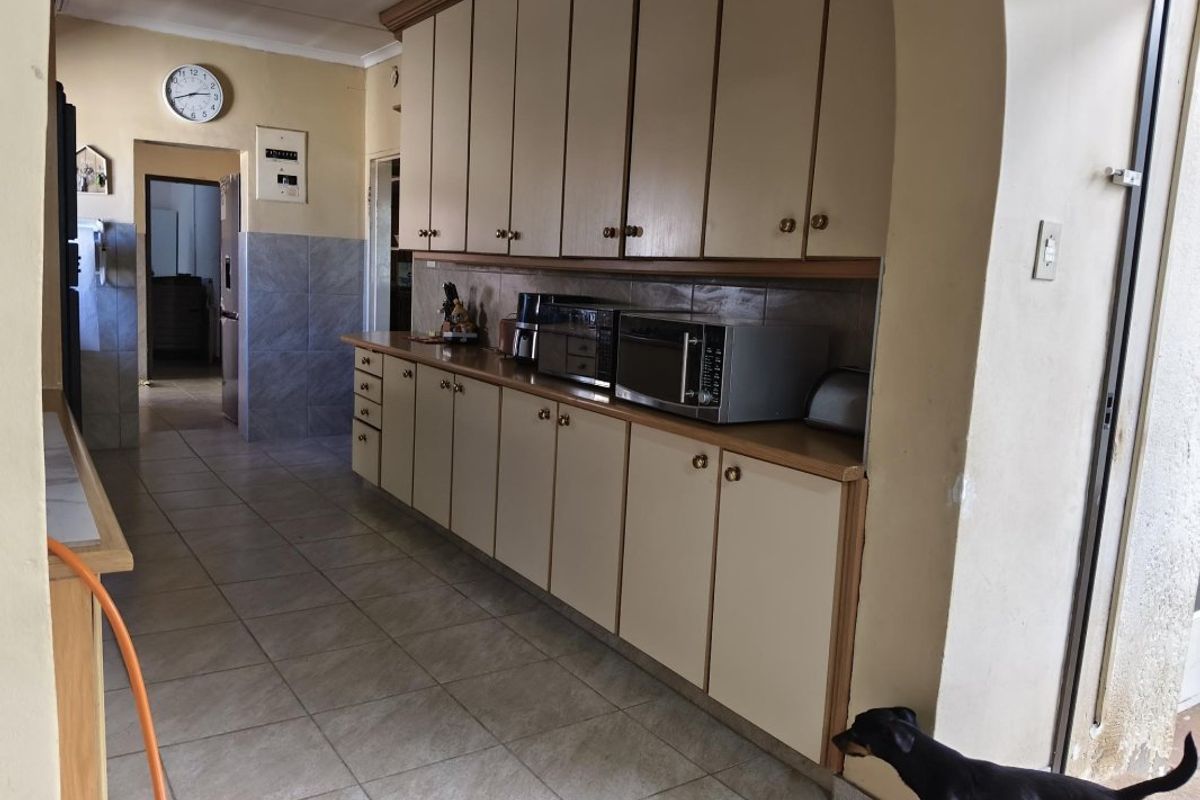 A functional kitchen featuring extensive built-in cabinetry, tiled flooring, and a tiled splashback, offering a dated aesthetic ready for modernization.