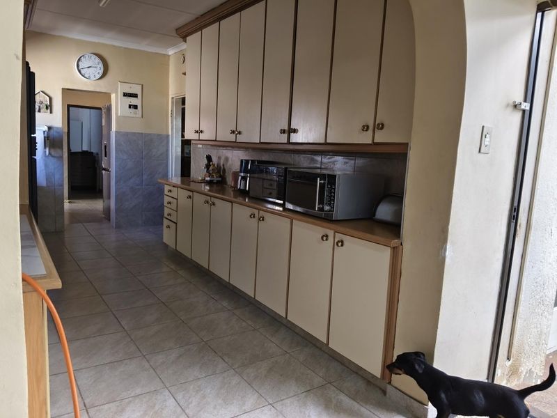 A functional kitchen featuring extensive built-in cabinetry, tiled flooring, and a tiled splashback, offering a dated aesthetic ready for modernization.