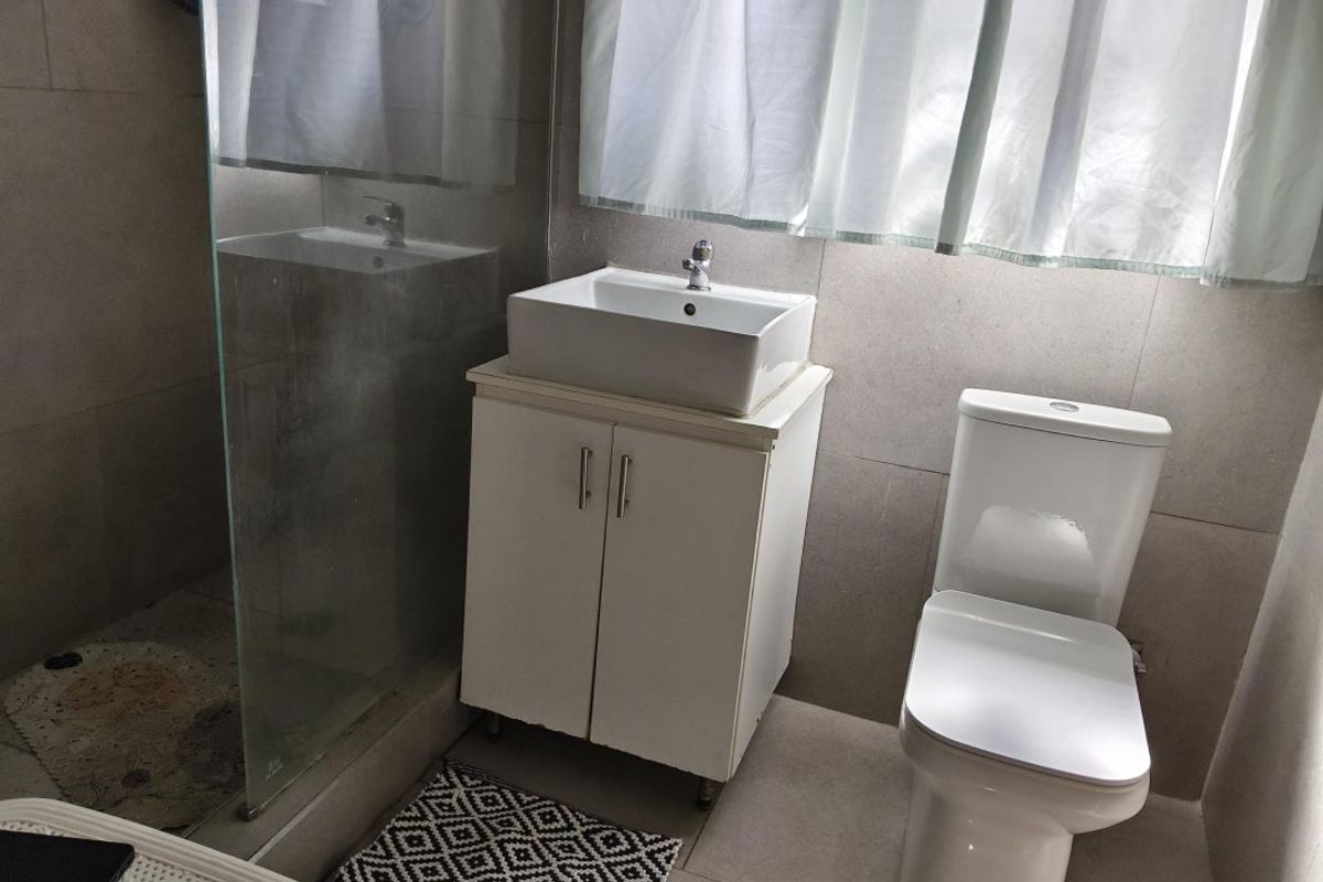 A functional bathroom featuring a vessel sink with vanity cabinet, a modern toilet, and a glass-enclosed shower area with neutral wall tiling.