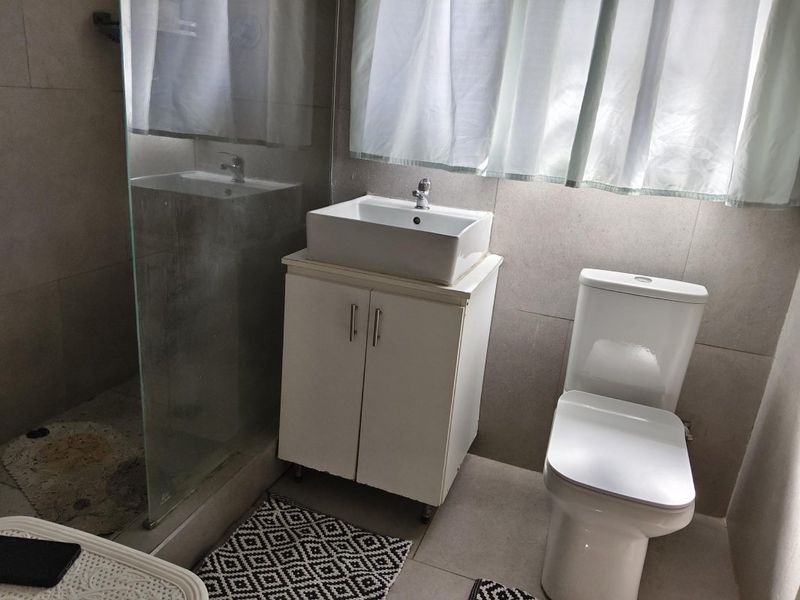 A functional bathroom featuring a vessel sink with vanity cabinet, a modern toilet, and a glass-enclosed shower area with neutral wall tiling.
