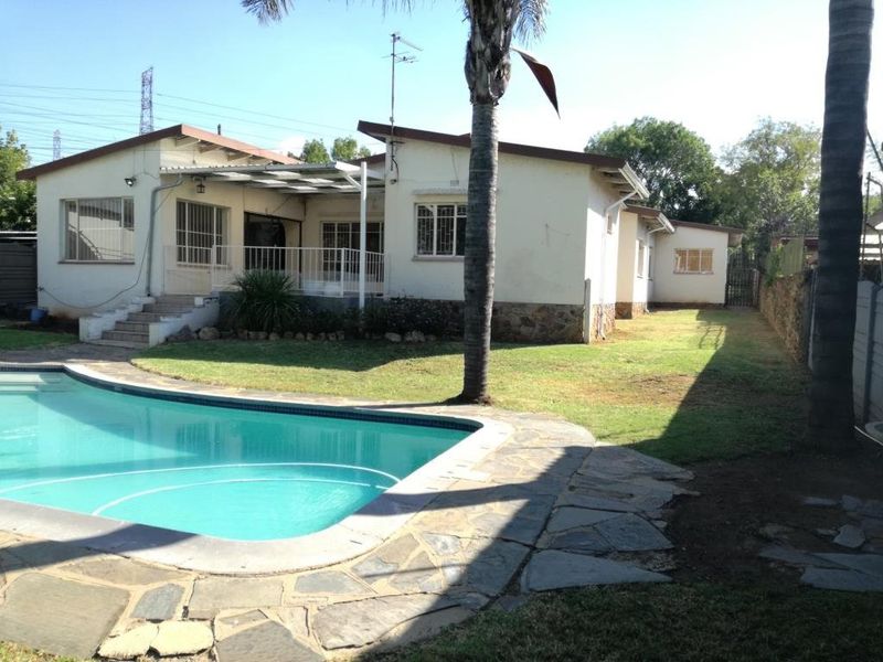 Rear view of the house featuring a swimming pool, stone paved patio area, and a covered outdoor space with established garden surroundings.