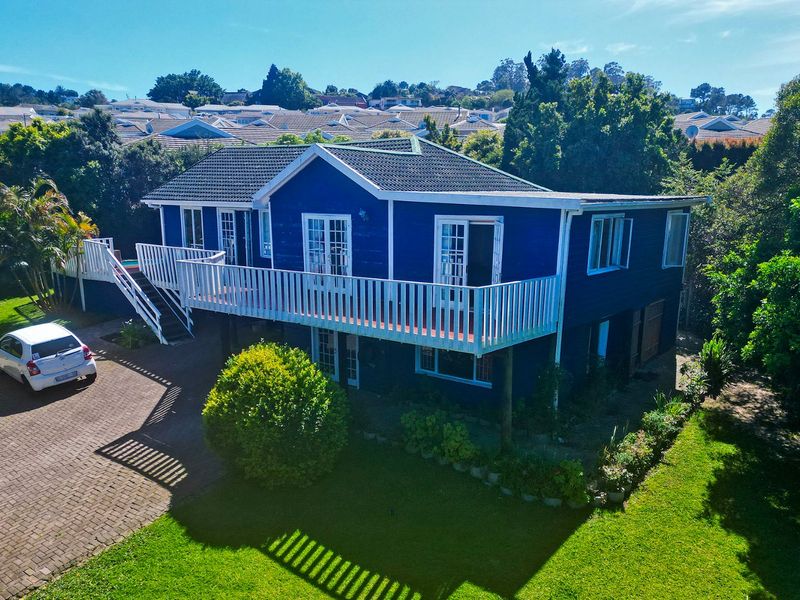 Aerial view of a blue-painted detached house featuring an elevated deck, paved driveway, and surrounding garden in a residential neighborhood.