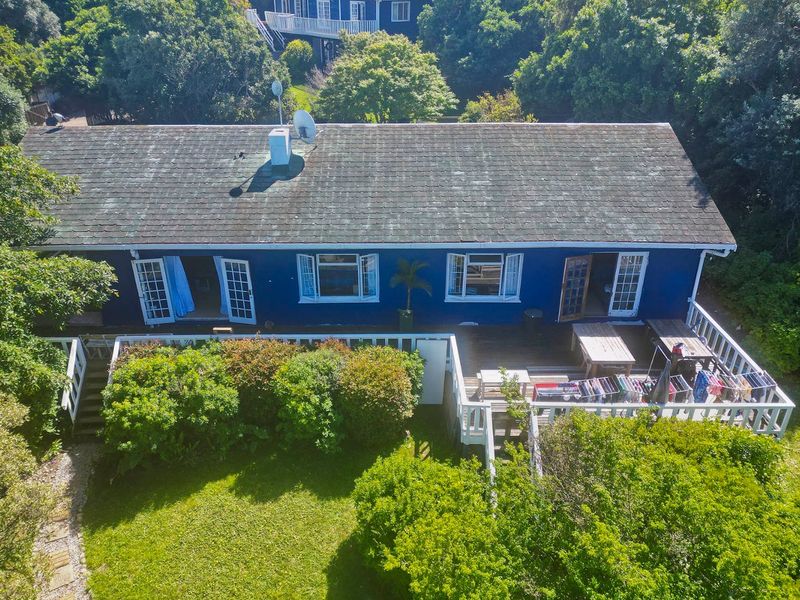 Aerial view of a blue-painted house featuring a large timber deck, shingle roof, and surrounding garden area.