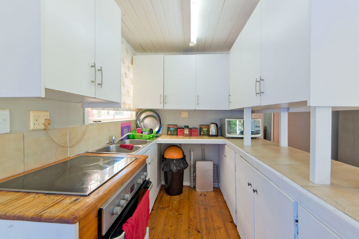 A functional galley-style kitchen featuring white cabinetry, timber countertops, an integrated electric hob and oven, and warm timber flooring.