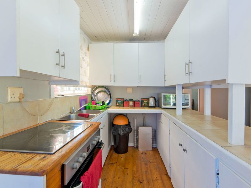 A functional galley-style kitchen featuring white cabinetry, timber countertops, an integrated electric hob and oven, and warm timber flooring.