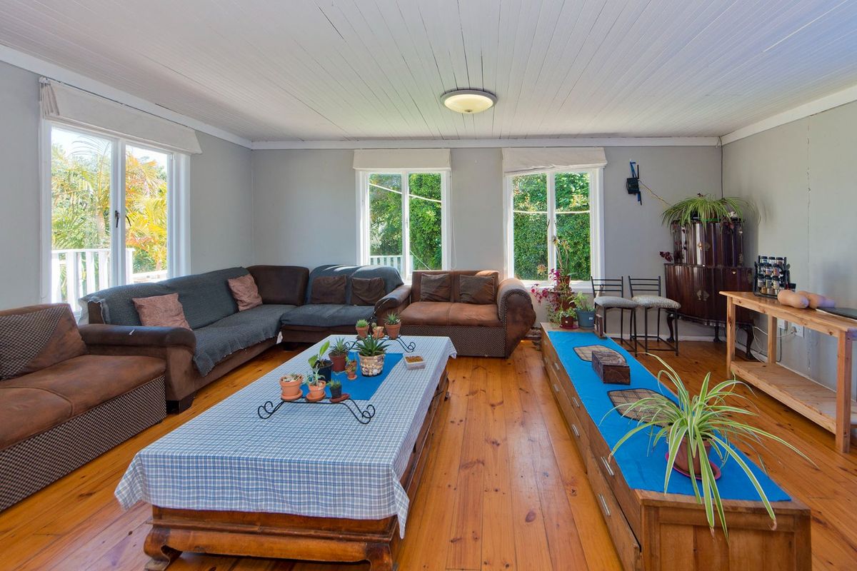 Spacious living room featuring polished timber flooring, a classic tongue and groove ceiling, and large windows providing ample natural light.